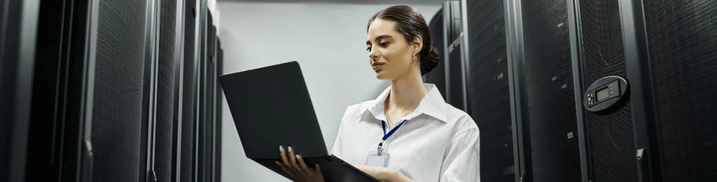 IT technician using a laptop by server racks